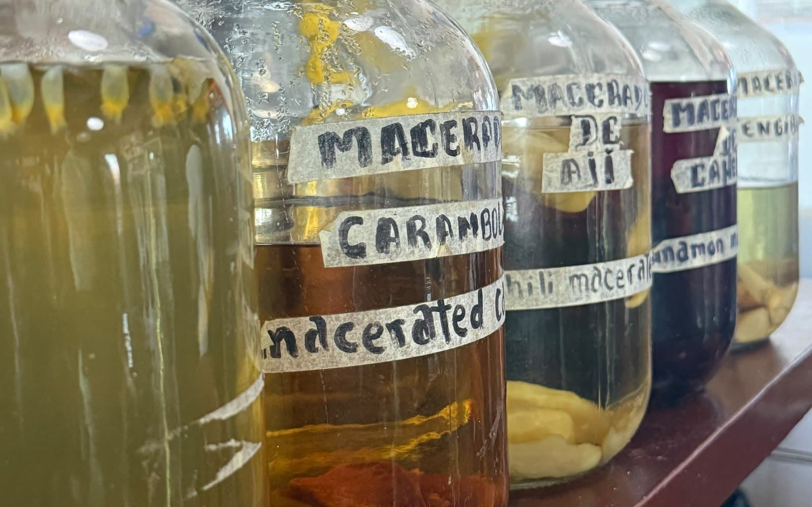 Garrafas de macerados de pisco —carambolo, ají, canela— en el restaurante Lucaffe, en Paracas, incluido en el tour, 6 de junio de 2026